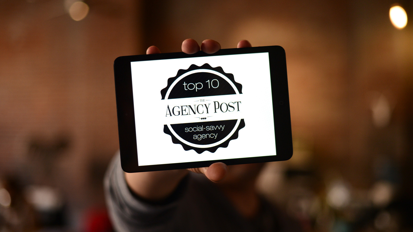 A person holding an iPad mini with Top 10 Social-Savvy Agency logo