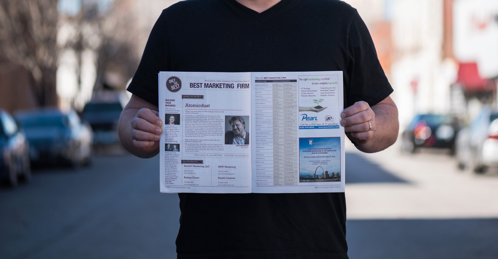 Atomicdust Creative Director Mike Spakowski holds a Small Business Monthly issue open to the Best Marketing Firm St.Louis page in the middle of the street.
