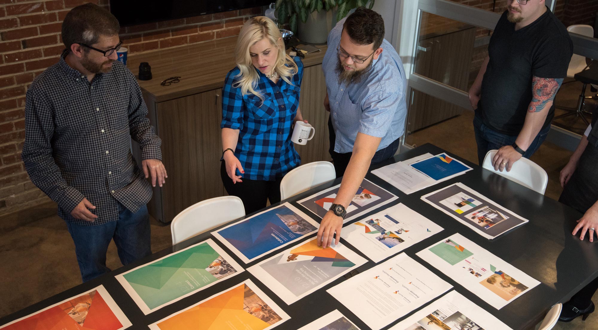 The creative team at Atomicdust discussing the a branding project with design print outs on the conference room table.