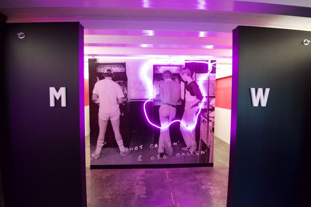 The restrooms at Start Bar with vintage arcade photography and pink neon glow