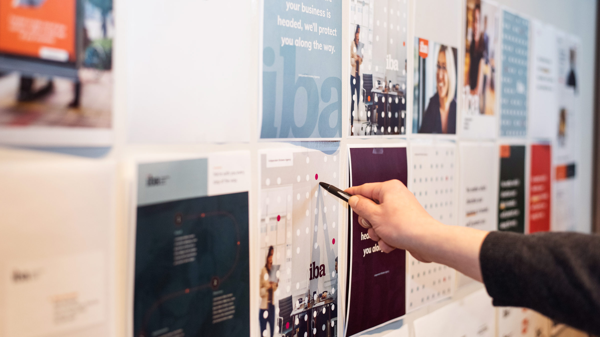 Designer at Atomicdust discuss branding elements for IBA insurance brokers on a whiteboard.