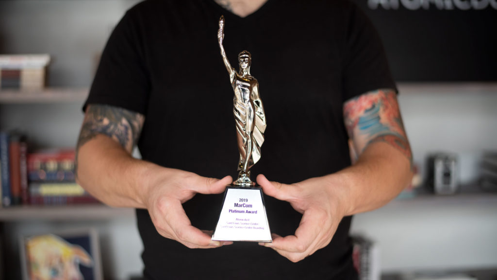 Atomicdust team member holding MarCom Award trophy