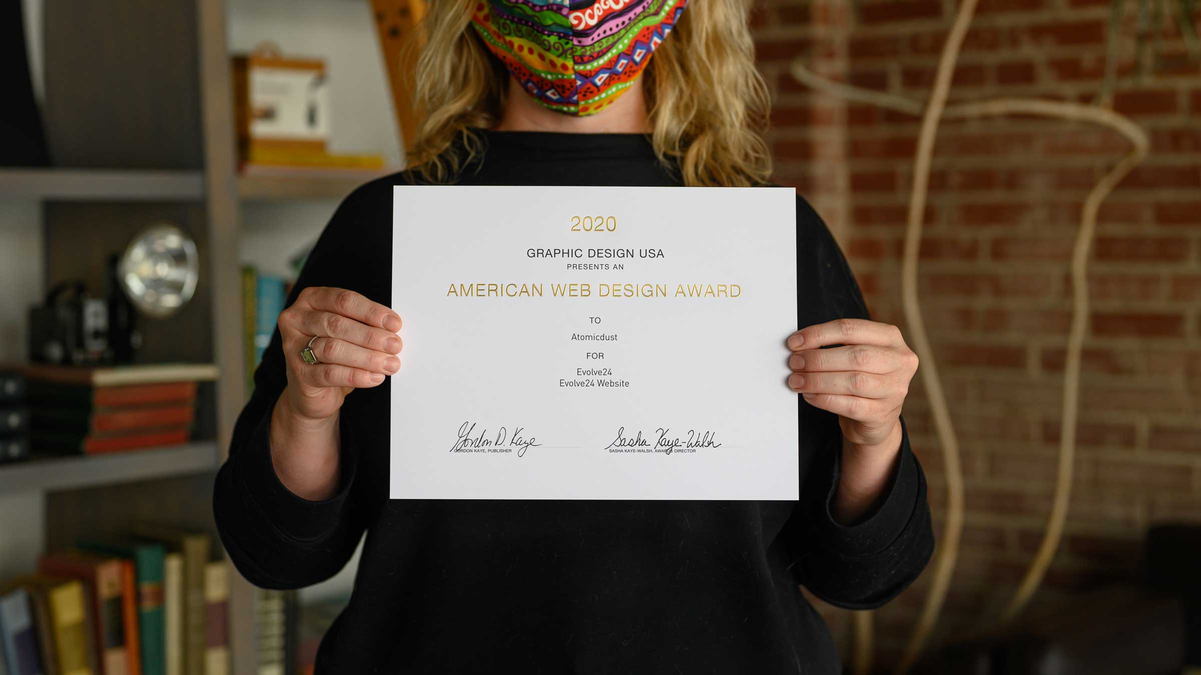 An Atomicdust team member holds a certificate from GDUSA's 2020 American Web Design Awards