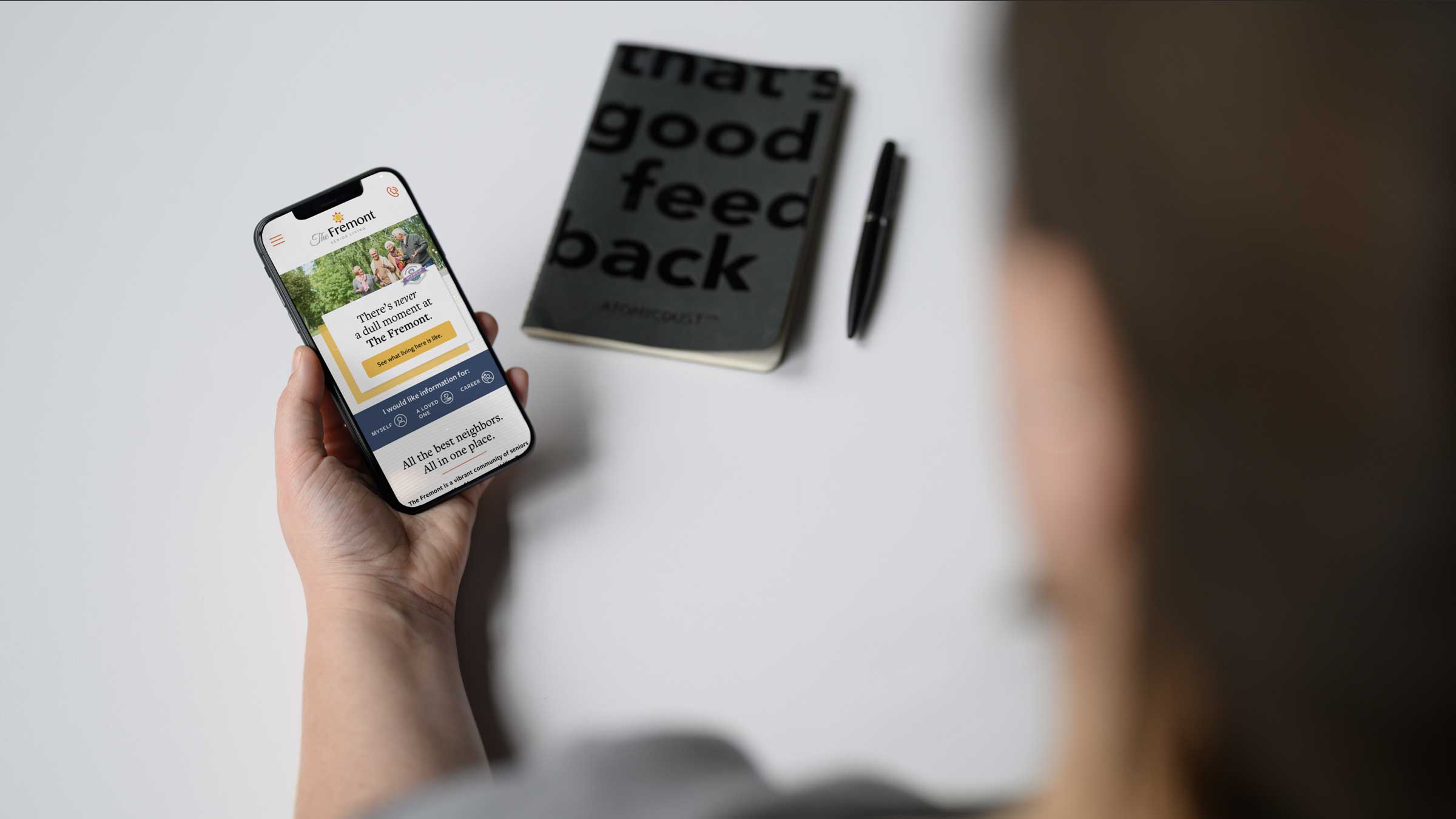 An Atomicdust team member holds an iPhone looking at the Arrow Senior Living website design