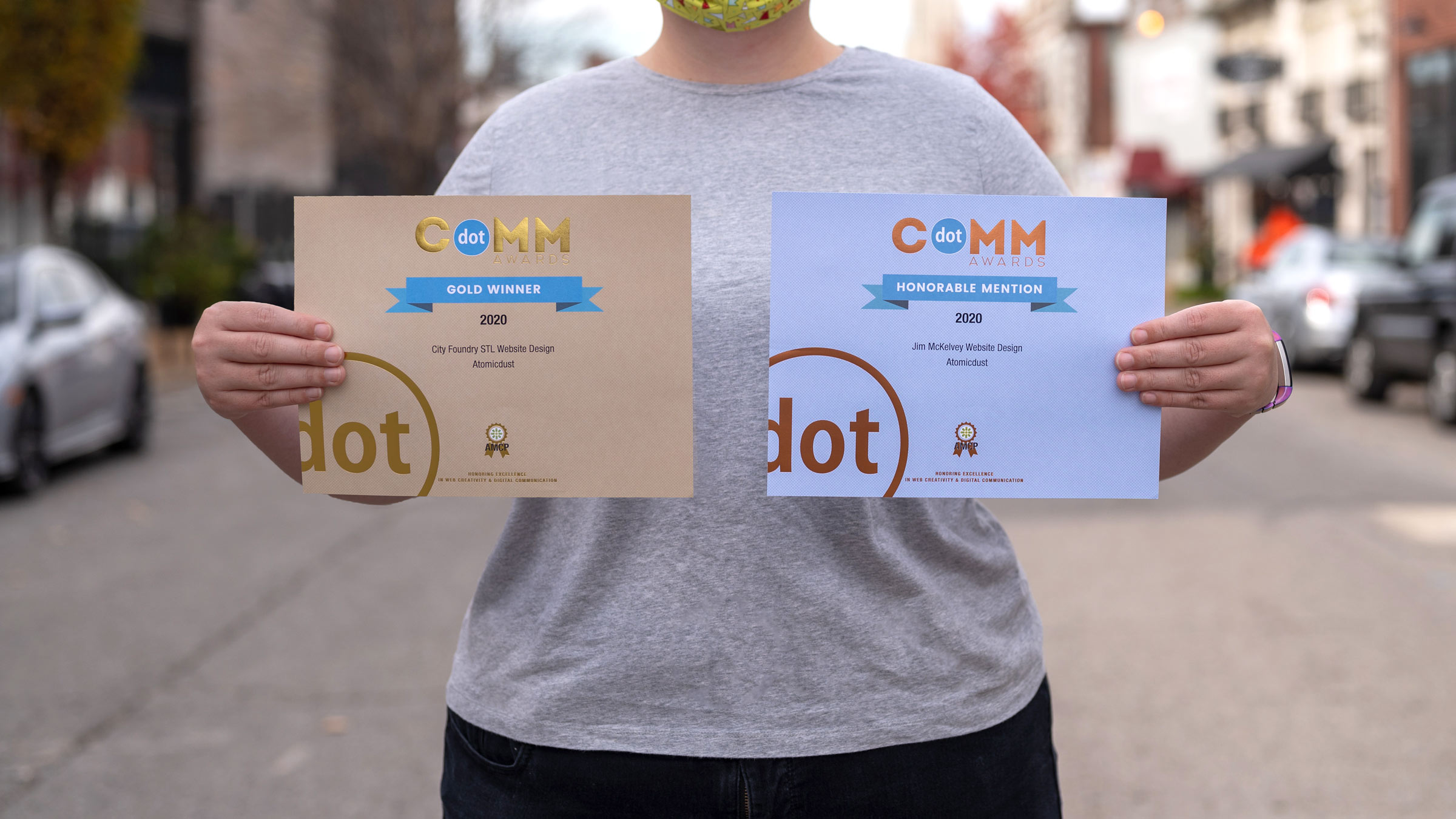 An Atomicdust team member holds two dotCOMM Awards for web design