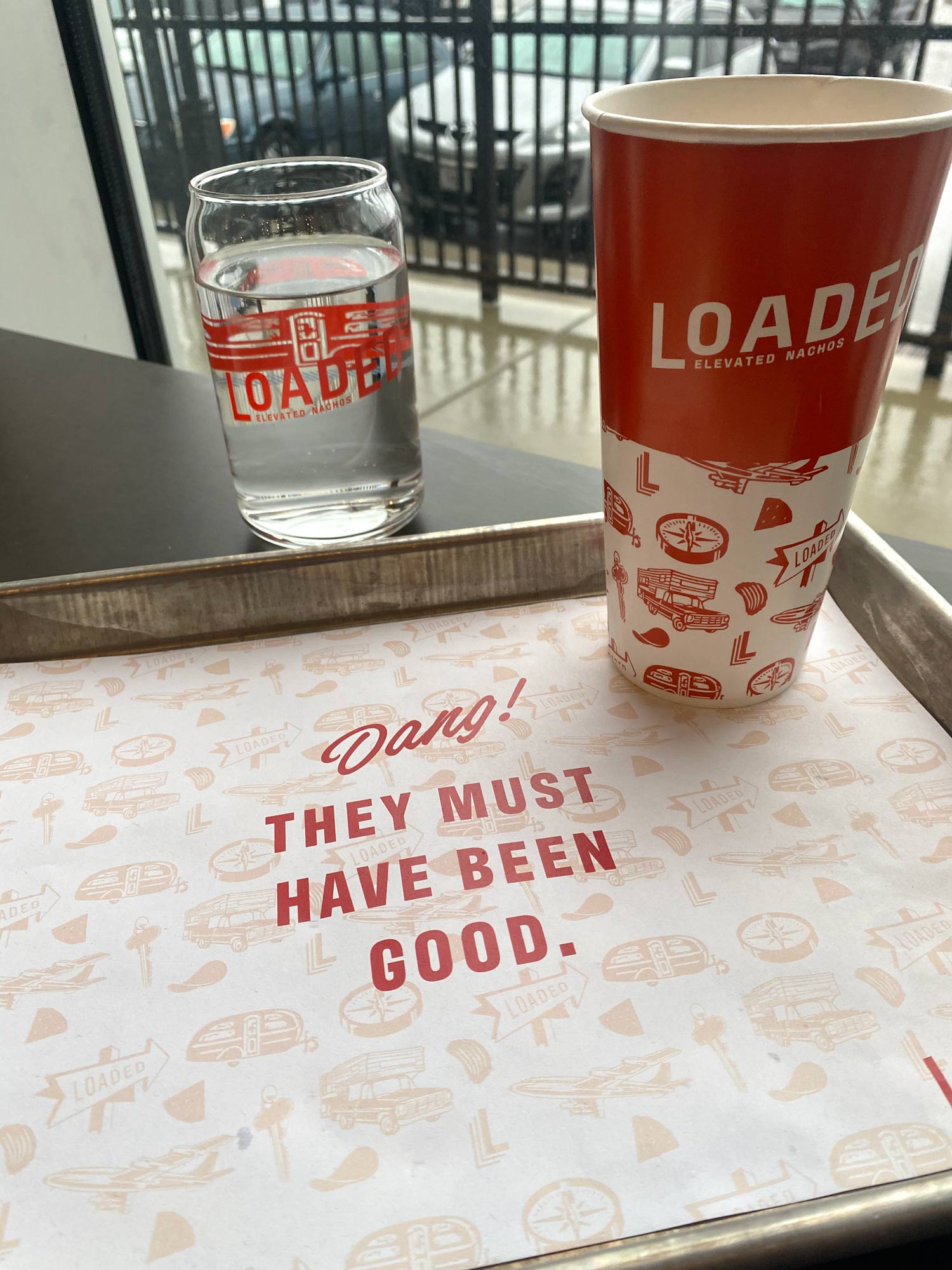Tray paper that says "Dang! They must have been good," glass cups and paper cups as part of Loaded's fast-casual branding