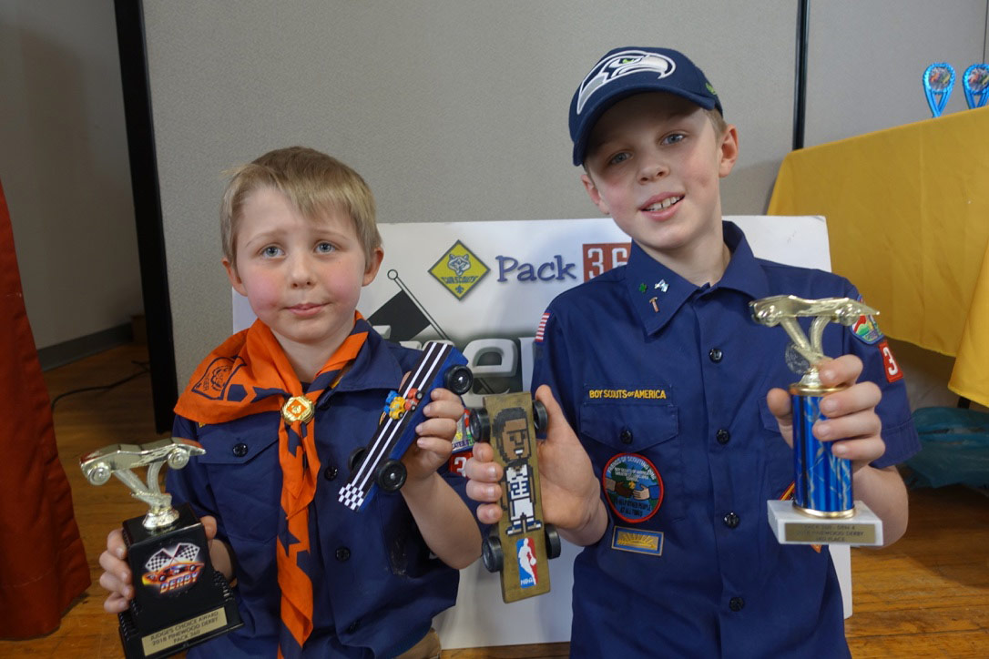 Boys hold Pinewood Derby cars and trophies