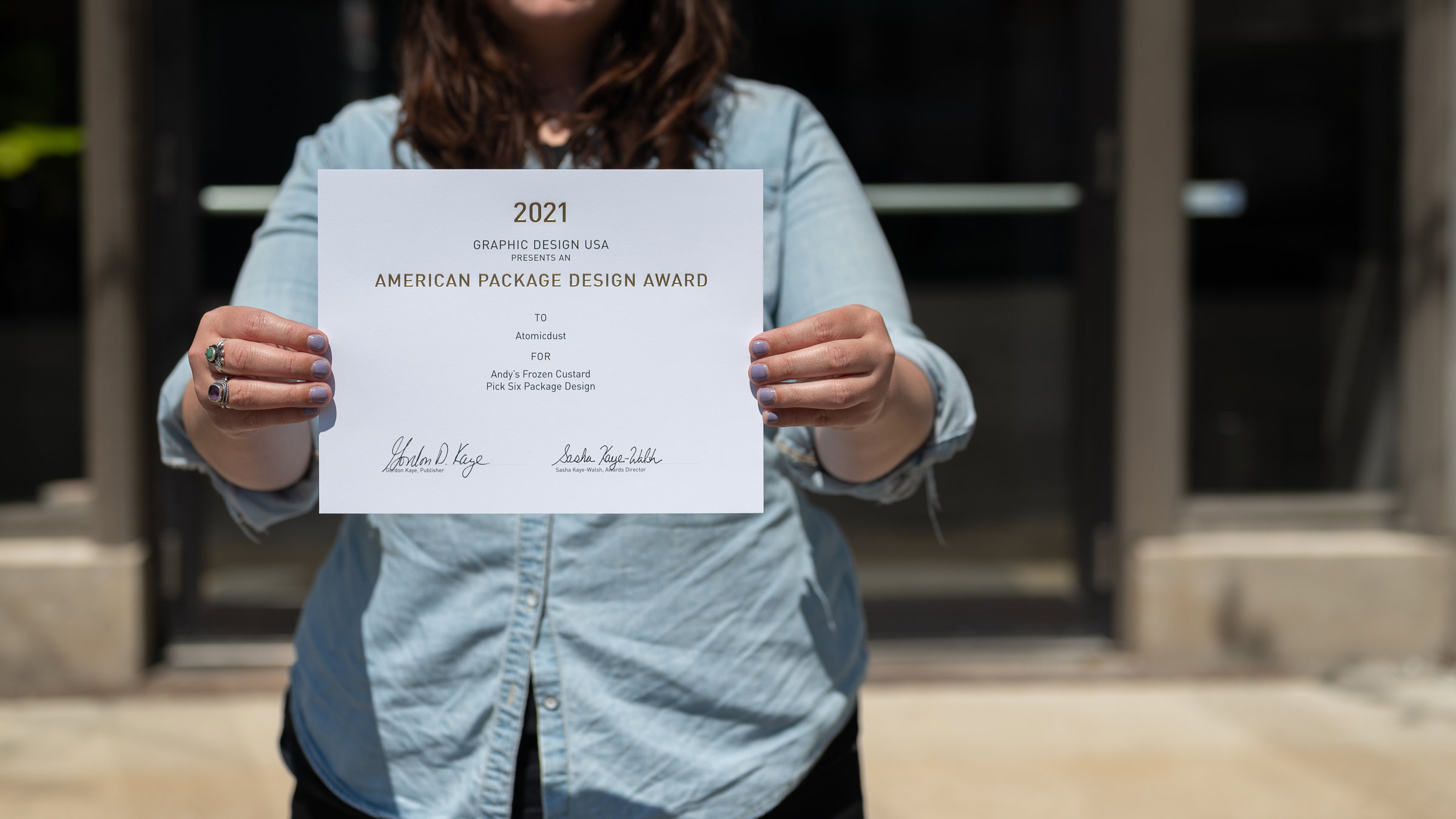 A team member holds the GDUSA Packaging Design Awards certificate