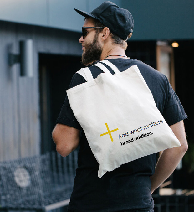 Man holds a tote bag with brand addition branding