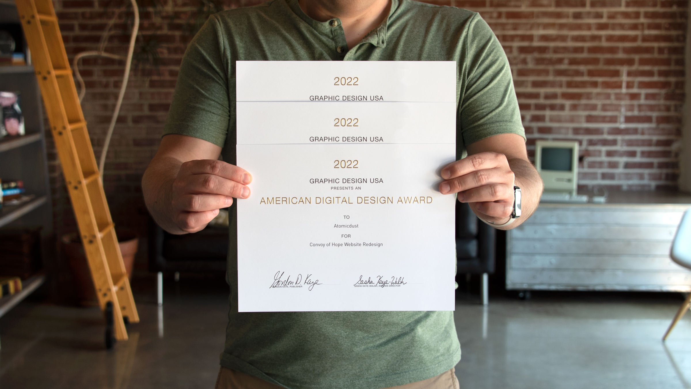 An Atomicdust team member holds this year's GDUSA Digital Design Awards certificates