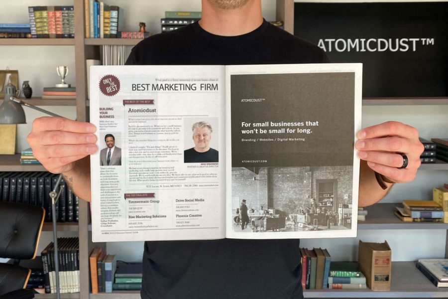 An Atomicdust team member holds the Small Business Monthly issue announcing Atomicdust as Best Marketing Firm