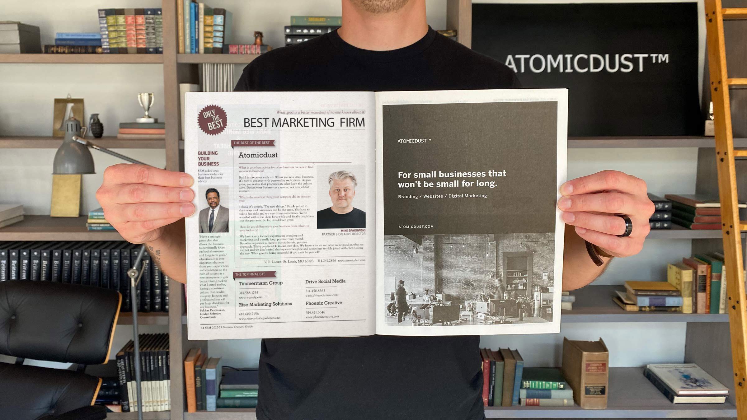 An Atomicdust team member holds the Small Business Monthly issue announcing Atomicdust as Best Marketing Firm