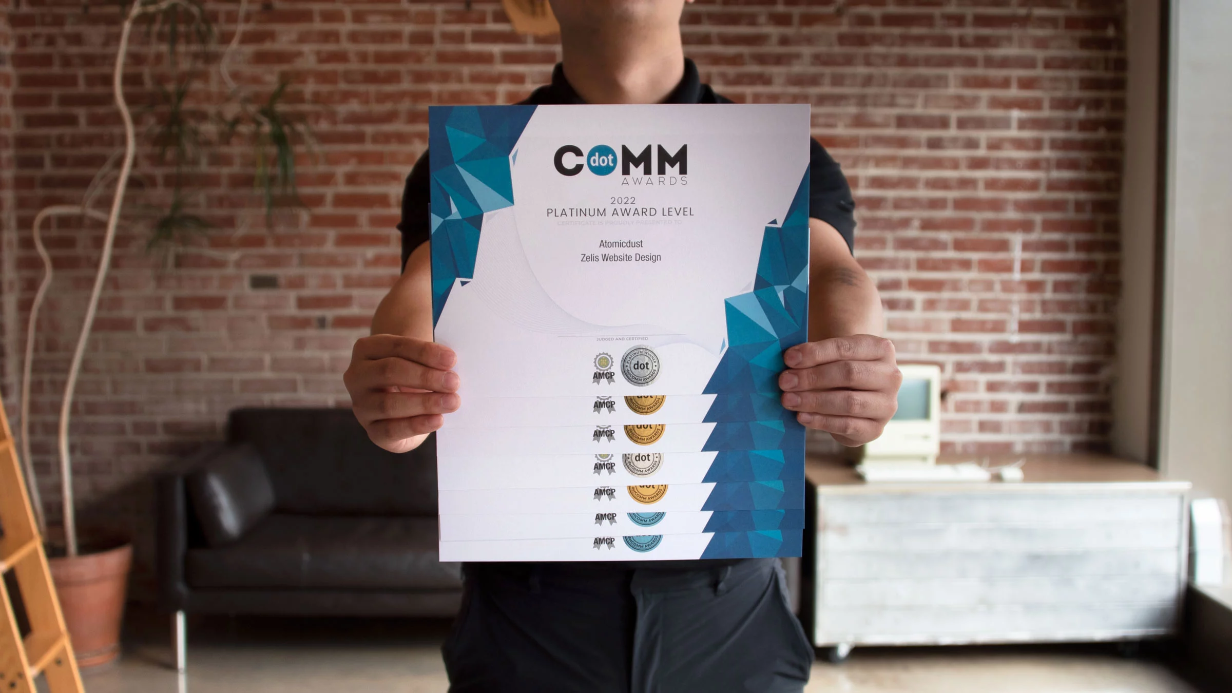 Atomicdust team member holds seven 2022 dotComm Awards certificates for website design