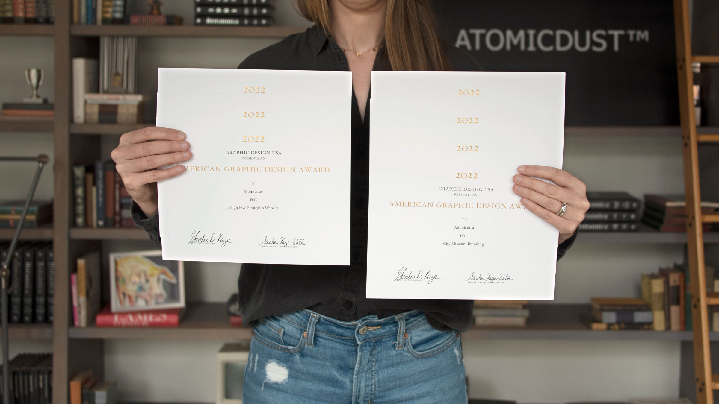 An Atomicdust team member holds seven Graphic Design USA American Design Awards