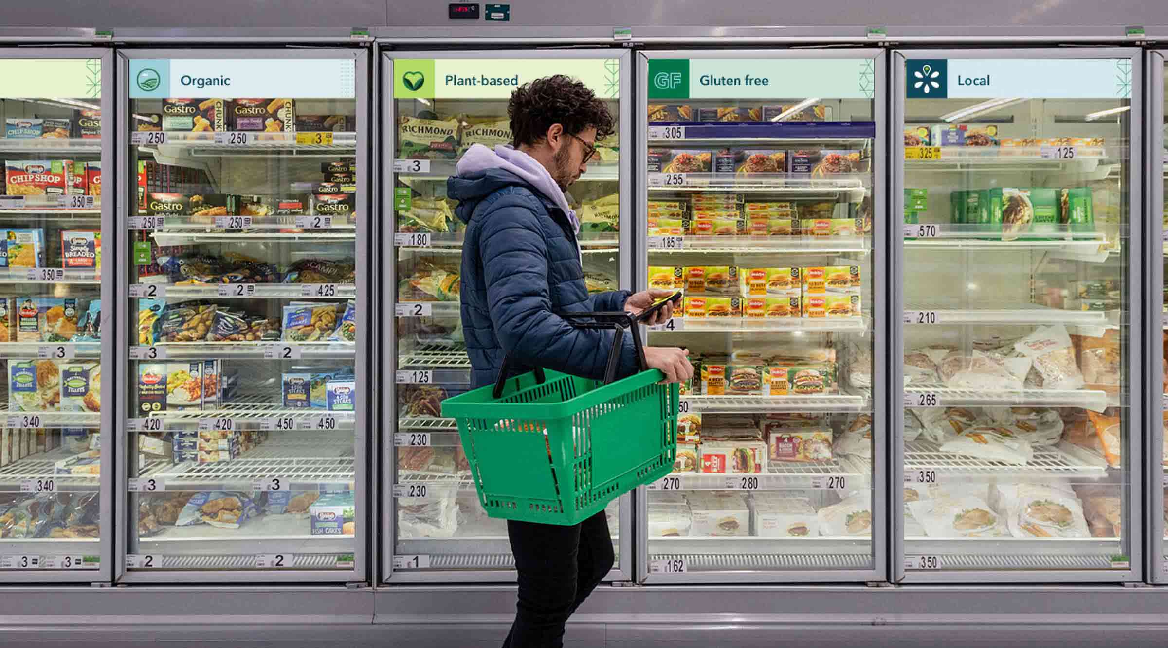 A person walks past the freezer aisle of the grocery store with Eatwell branding on signage