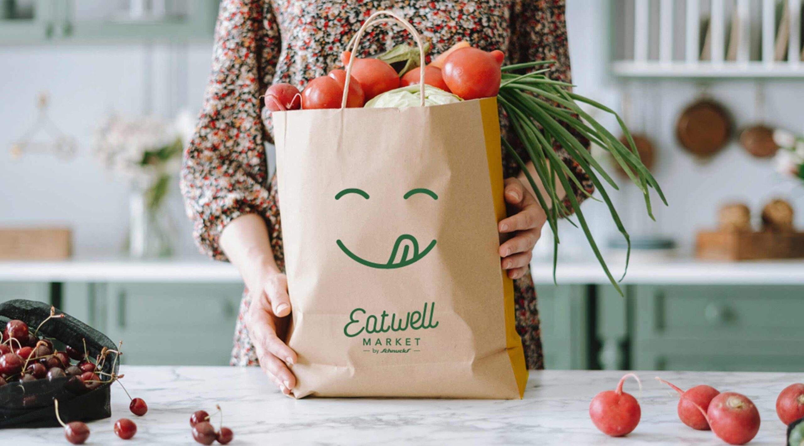 A person places an Eatwell Markets-branded paper grocery bag on the kitchen counter