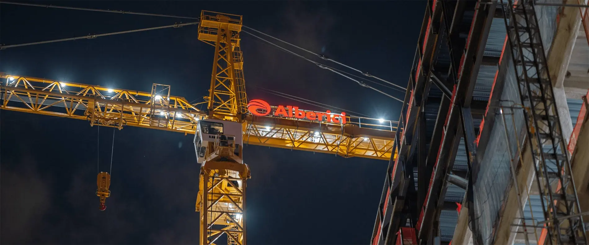 A construction crane, lit up at night, with the Alberici branding