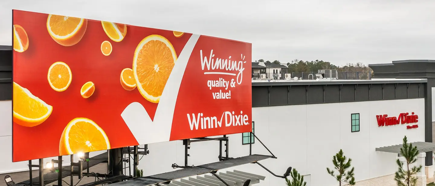 A billboard with Winn-Dixie's grocery store marketing, featuring oranges and text that says "Winning quality and value. Winn-Dixie!"