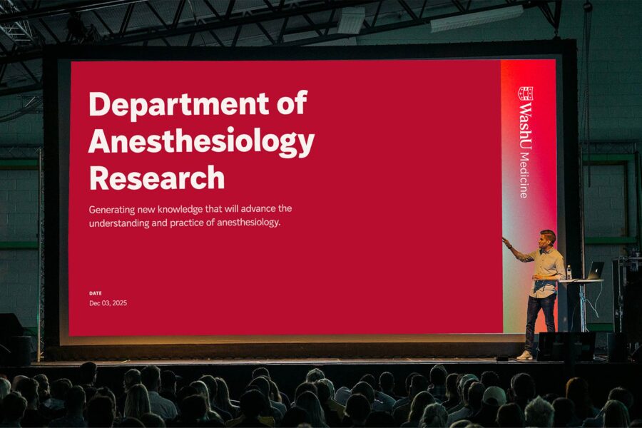 A speaker gives a talk at a conference with the WashU Medicine brand identity on a huge screen