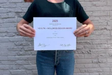 An Atomicdust team member holds a 2025 Graphic Design USA Health + Wellness Awards certificate