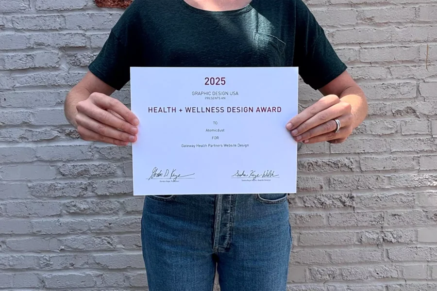 An Atomicdust team member holds a 2025 Graphic Design USA Health + Wellness Awards certificate