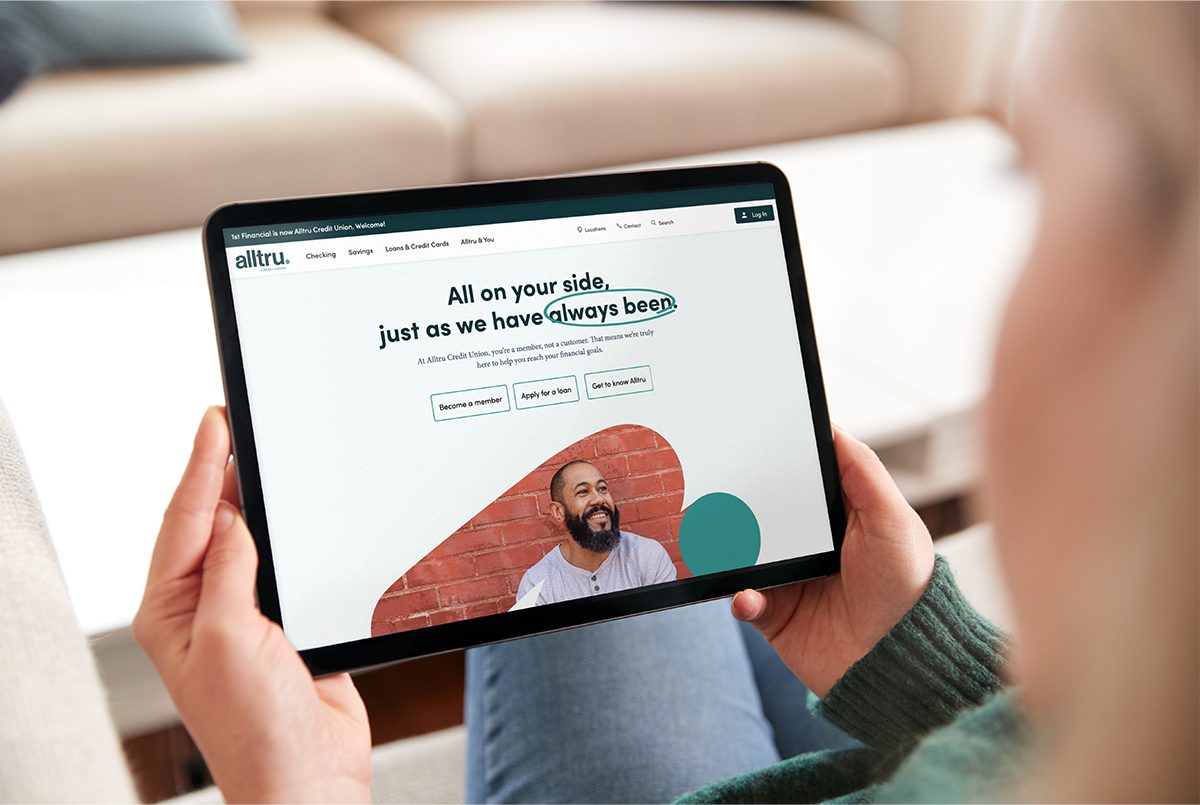 A person holds a tablet looking at the Alltru Credit Union web design