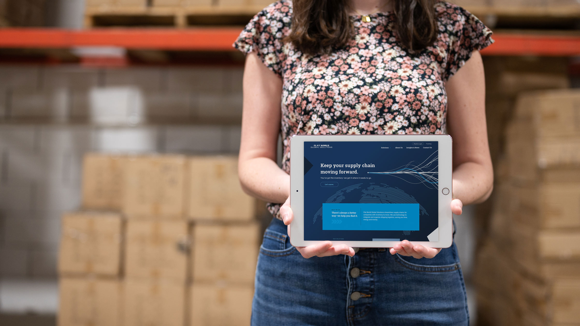 A woman in a warehouse holds an iPad with the Flat World website design on it