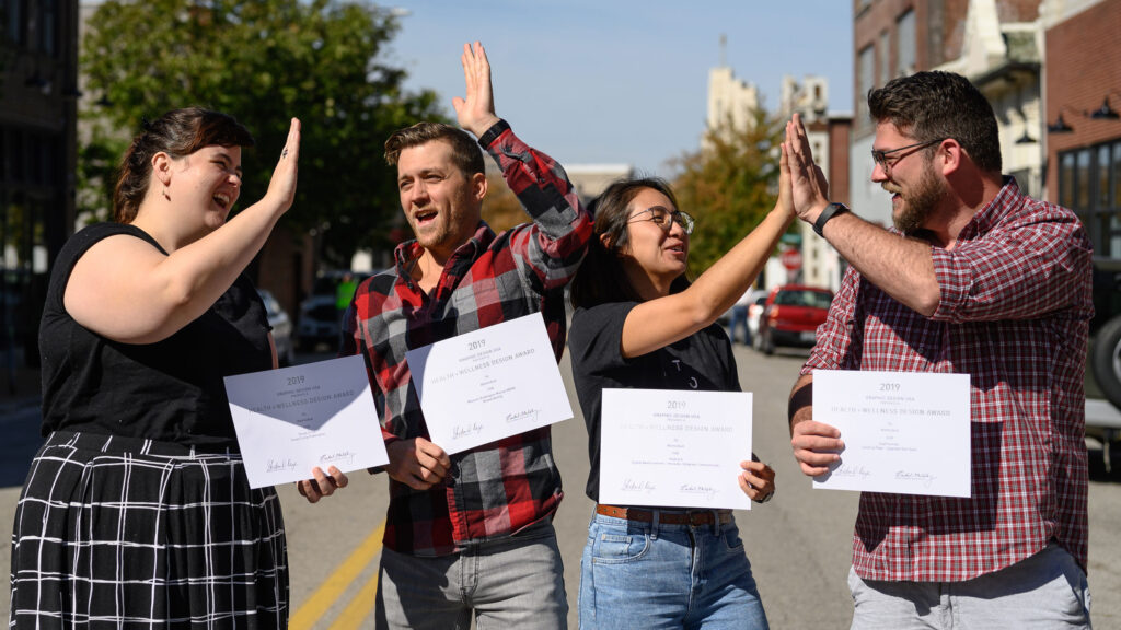 Atomicdust team members holding GDUSA Health + Wellness Awards certificates and high-fiving