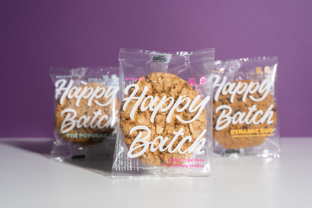 Three Happy Batch cookies in the packaging against a purple background