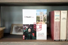 WashU Law admissions brochure displayed on bookshelf featuring campus imagery and branded shield design by Atomicdust.