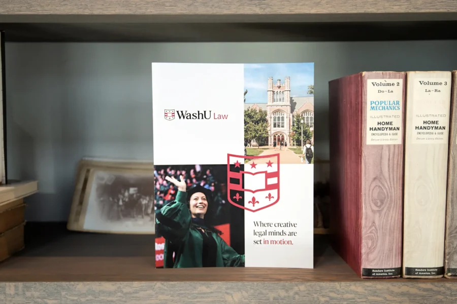 WashU Law admissions brochure displayed on bookshelf featuring campus imagery and branded shield design by Atomicdust.