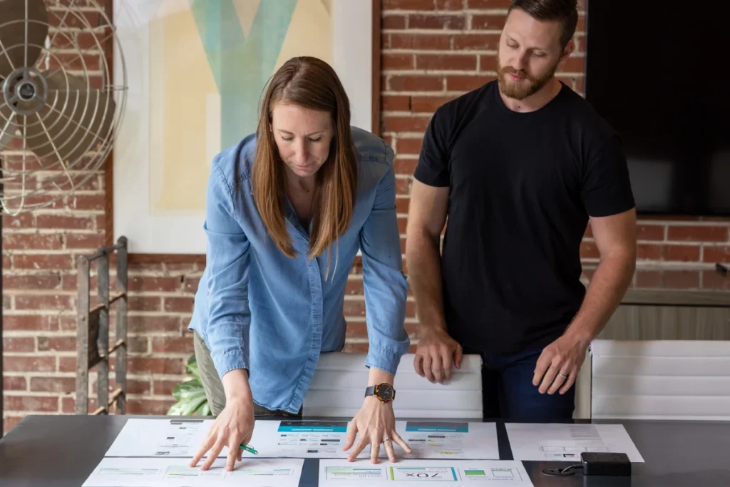 Two Atomicdust team members reviewing printed website wireframes in the studio