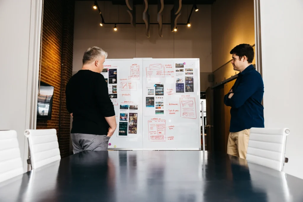 Two colleagues standing at a whiteboard covered in red website wireframe and sitemap sketches in the Atomicdust studio.