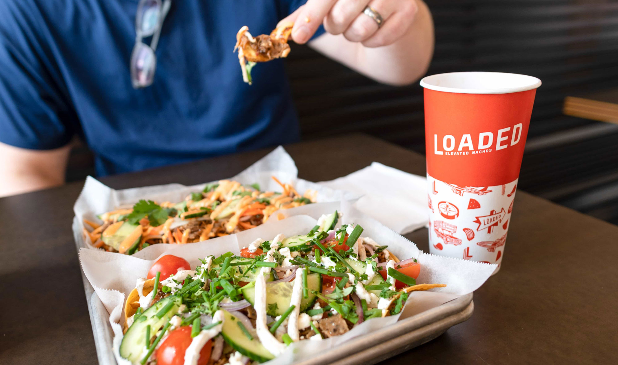 A man digs in to a tray of Loaded Elevated Nachos