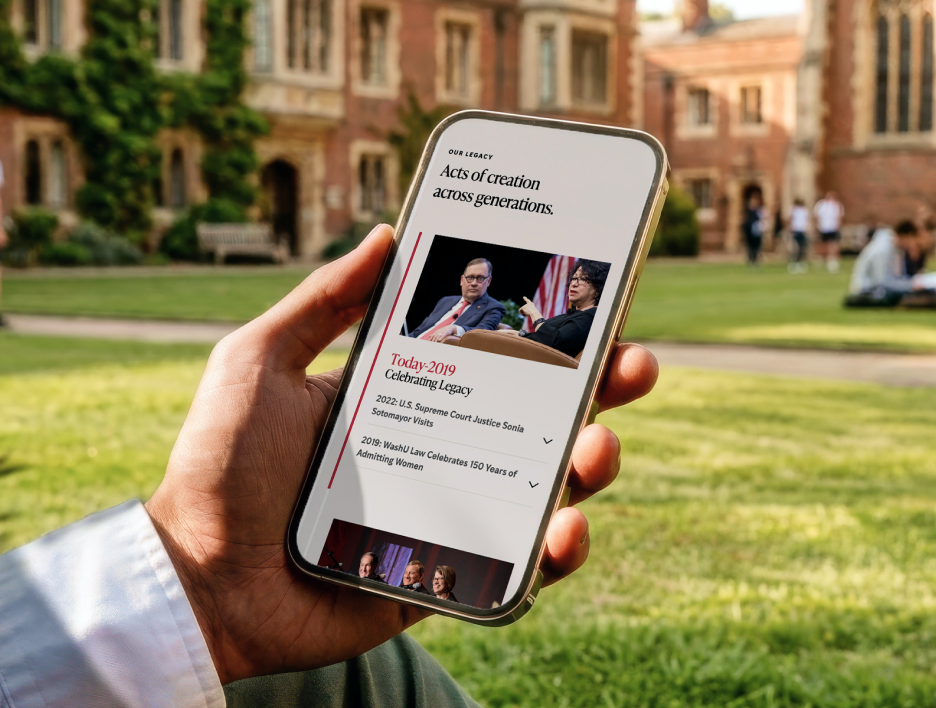 A student looking a the WashU Law digital timeline on their phone while sitting on the WashU Law campus.