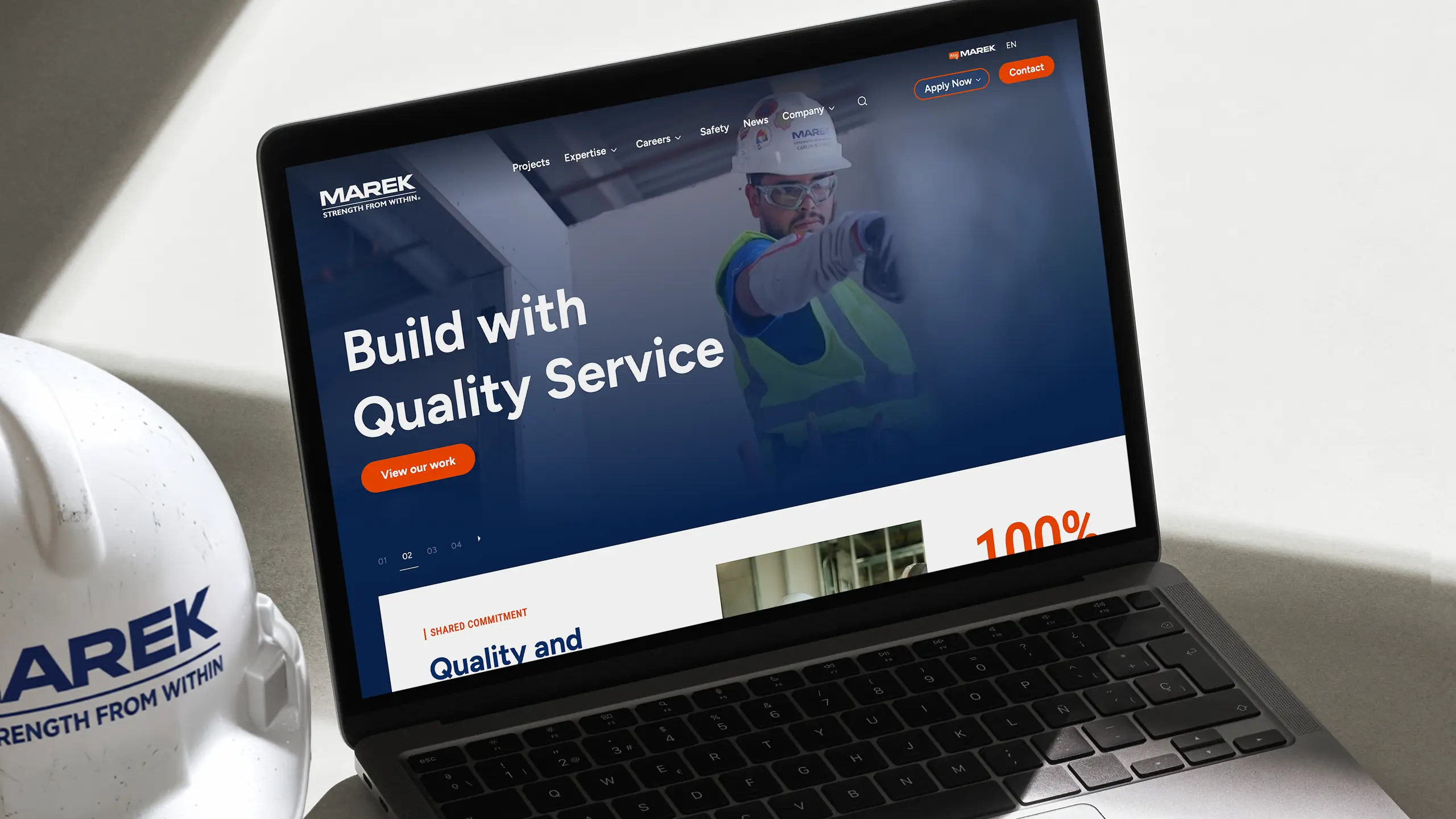 Laptop displaying the MAREK website homepage with the headline "Build with Quality Service" beside a MAREK hard hat