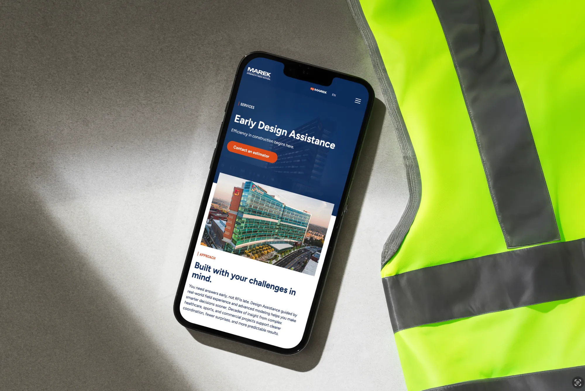 MAREK website service page displayed on a smartphone next to a safety vest