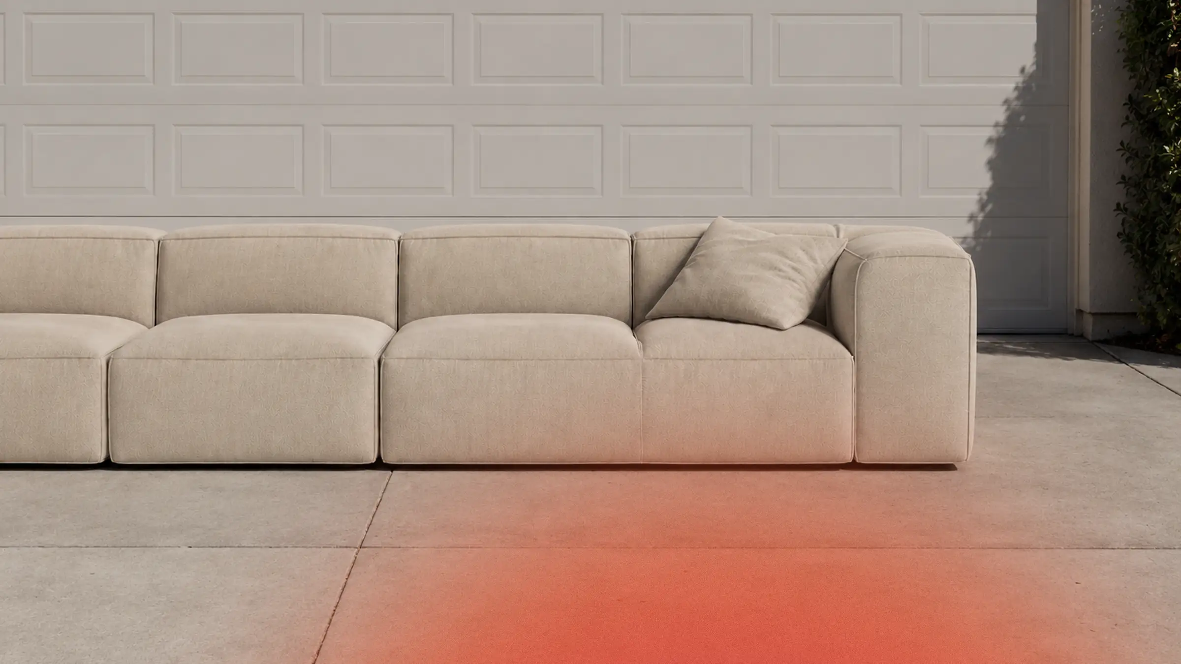 A beige sectional sofa sitting alone in a sunlit driveway in front of a closed white garage door, an orange glow washing across the concrete.