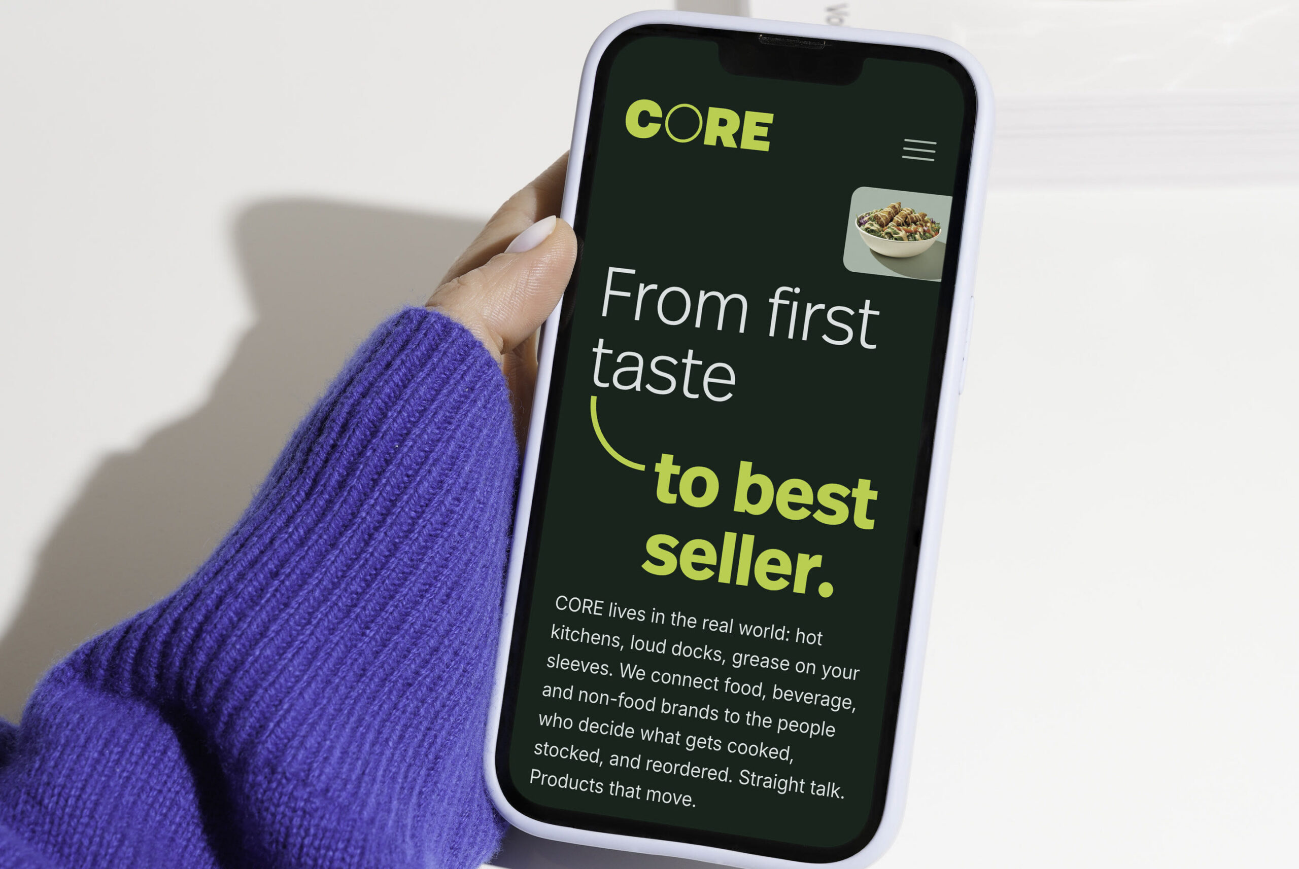 A hand holding a phone with the CORE website design pulled up