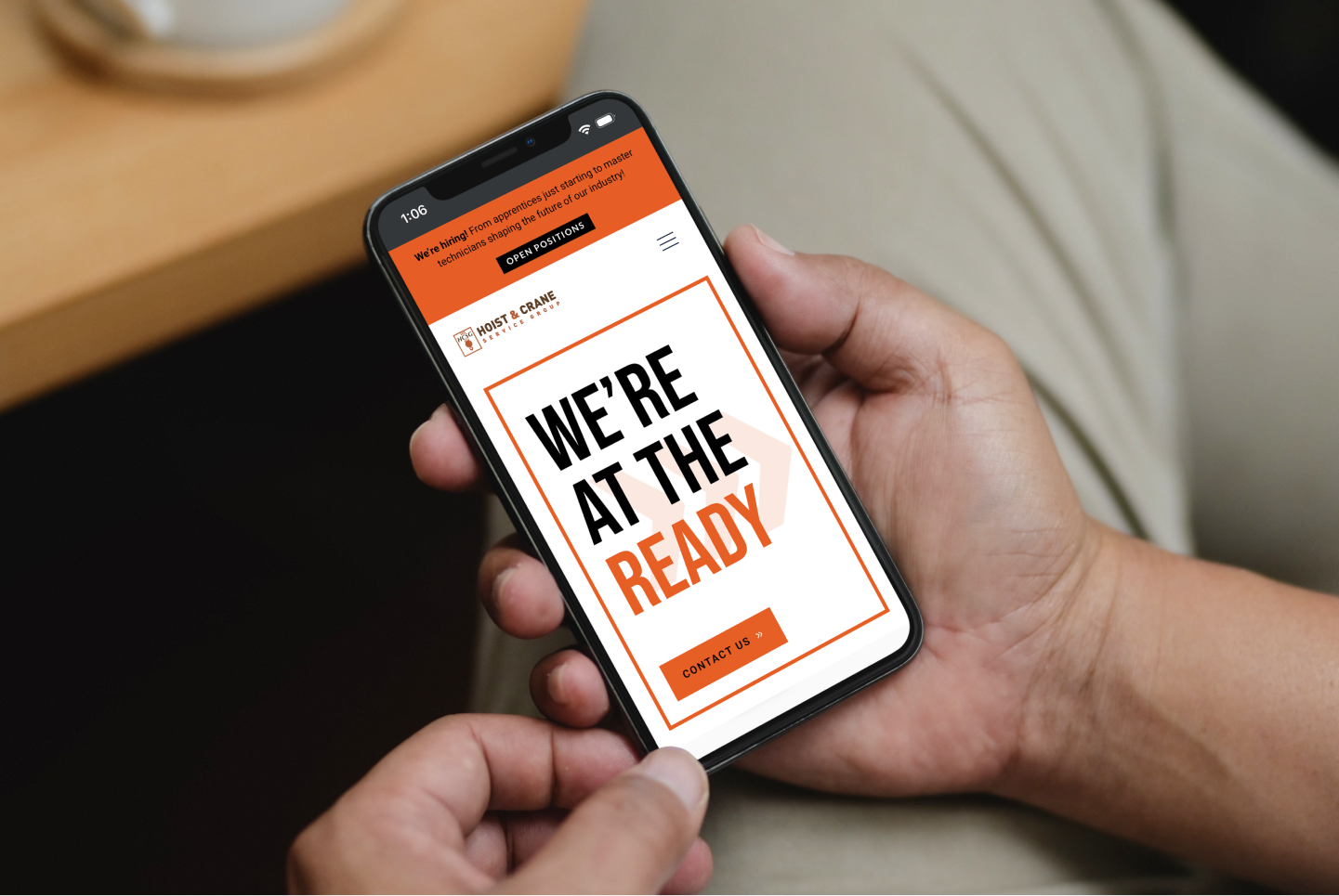 Hoist & Crane mobile website on a phone showing the "We're at the ready" headline, a contact button and a hiring banner