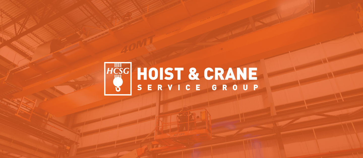 Hoist & Crane Service Group HCSG logo in white over an orange-toned photo of an overhead crane in a plant