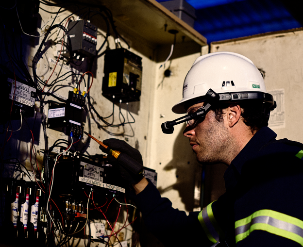 Hoist & Crane master technician in a hard hat testing wiring inside a crane control panel